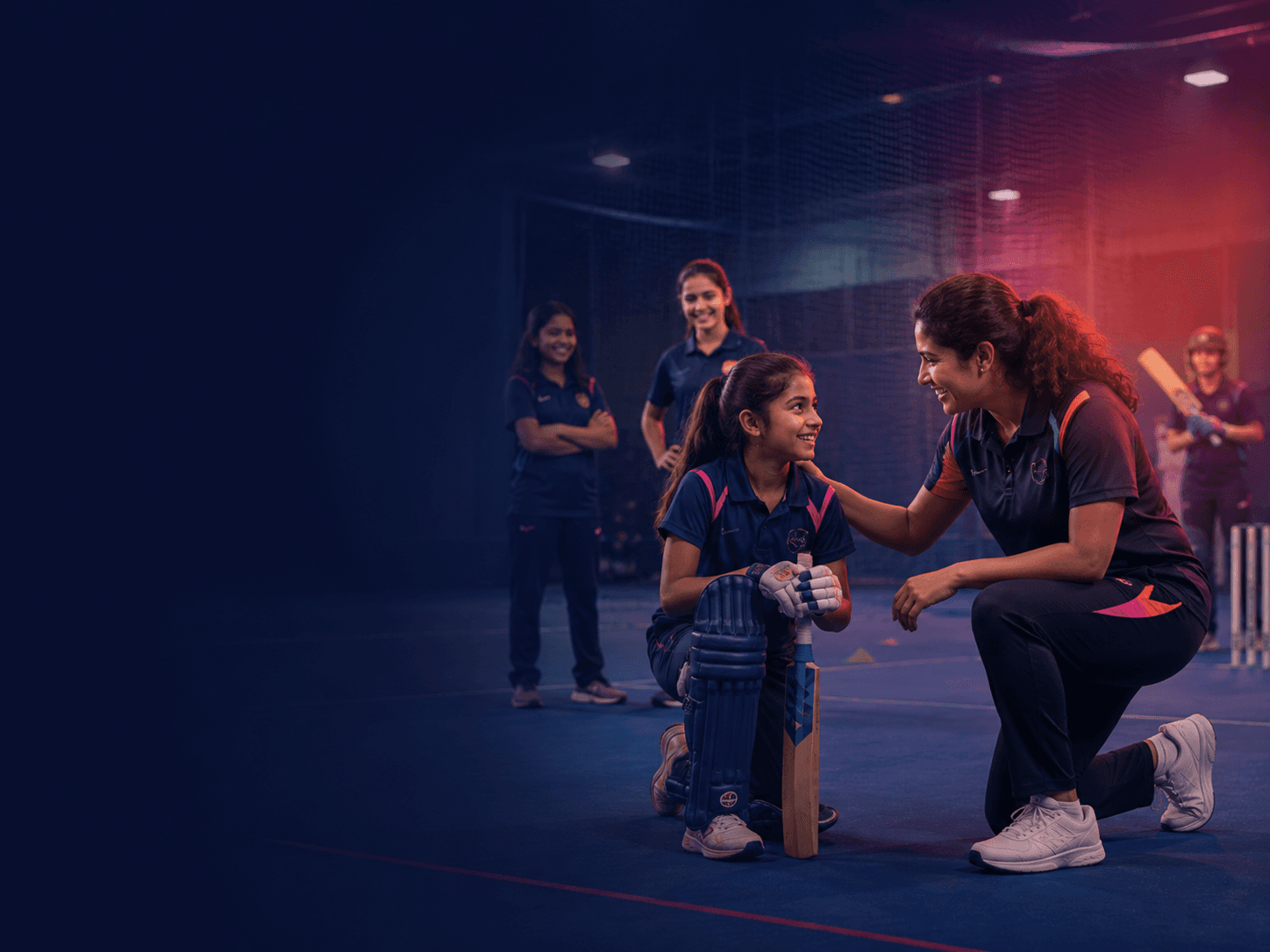 Indoor cricket coach encouraging a young player with teammates in the background
